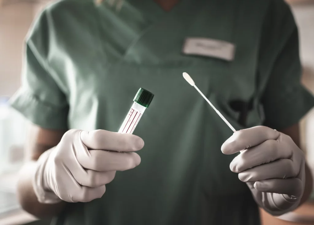 Gloved healthcare worker holding a swab and test tube used for medical sample collection