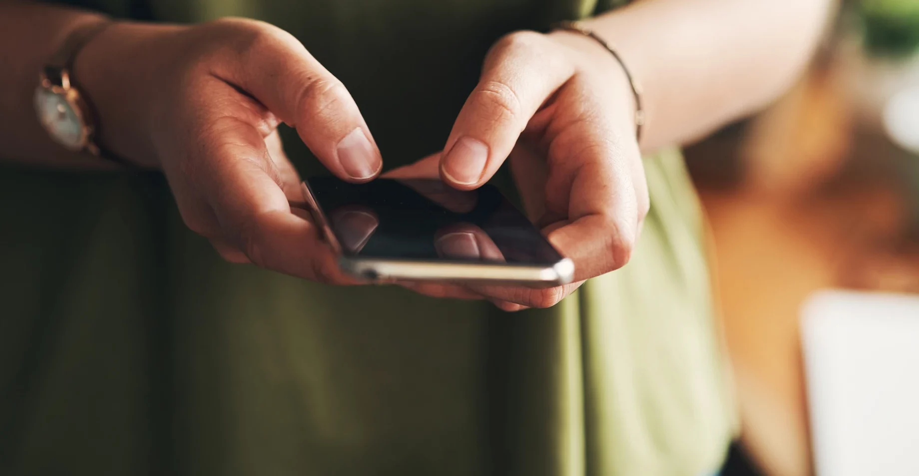 Close-up of a person's hands typing on a smartphone held between the fingers