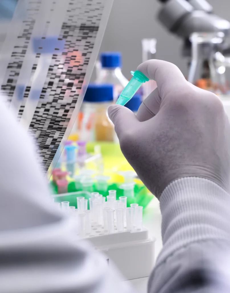 Gloved researcher holding a sample vial while examining a DNA sequencing gel in a laboratory