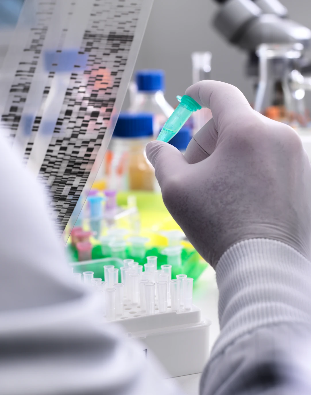 Gloved researcher holding a sample vial while examining a DNA sequencing gel in a laboratory
