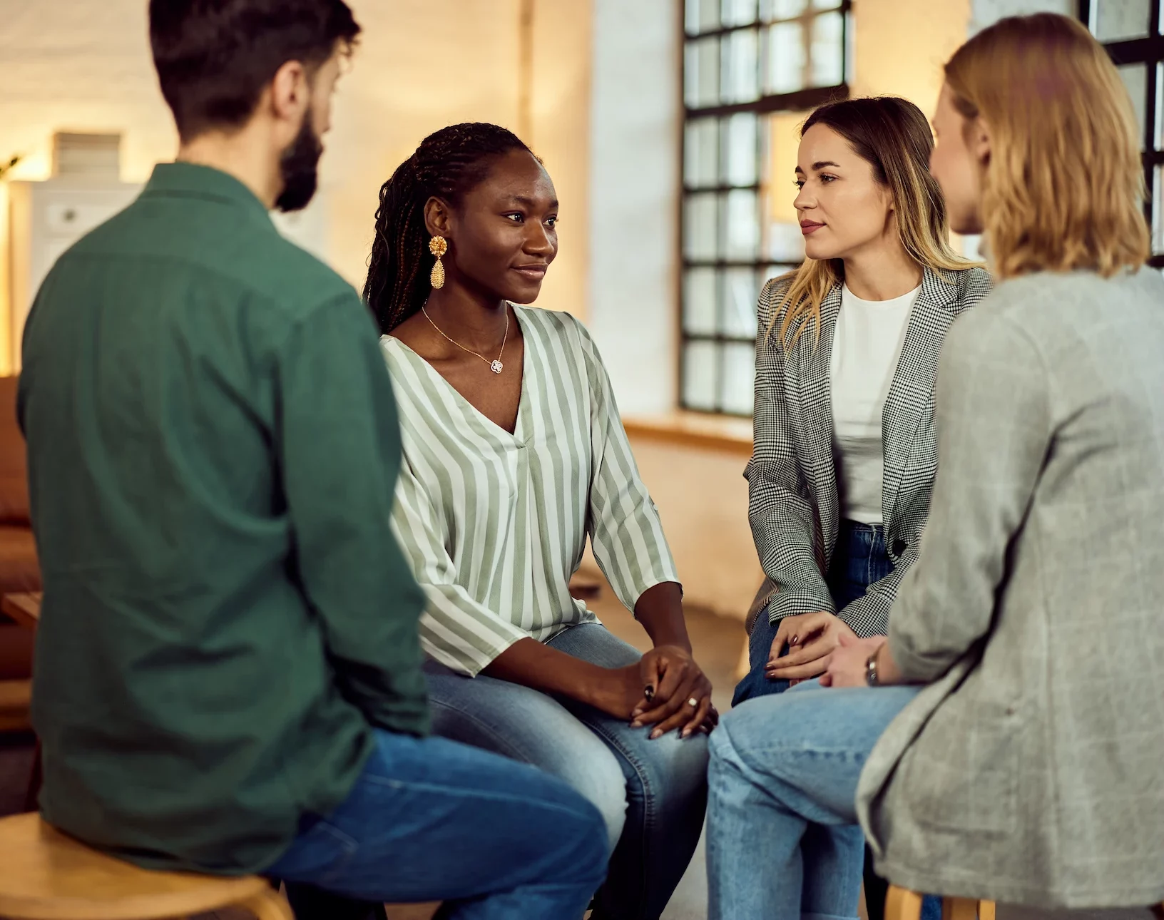 Four people sit in a circle on stools, engaged in conversation during a group discussion