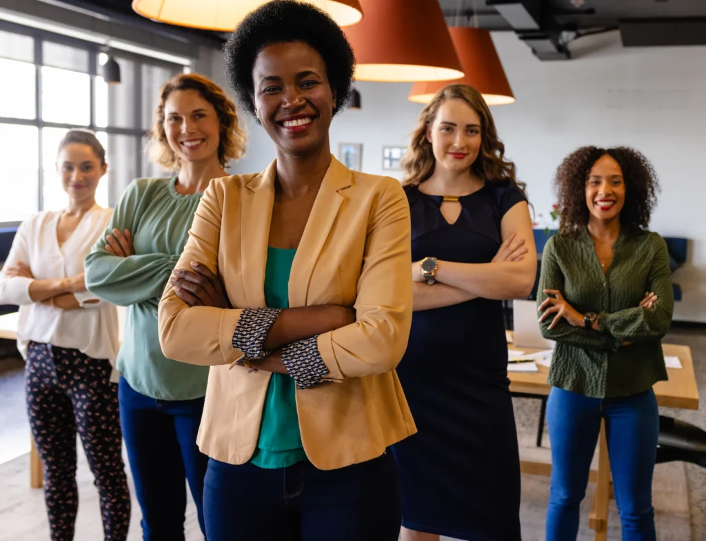 Five smiling businesswomen standing with arms crossed in a modern office, facing the camera confidently