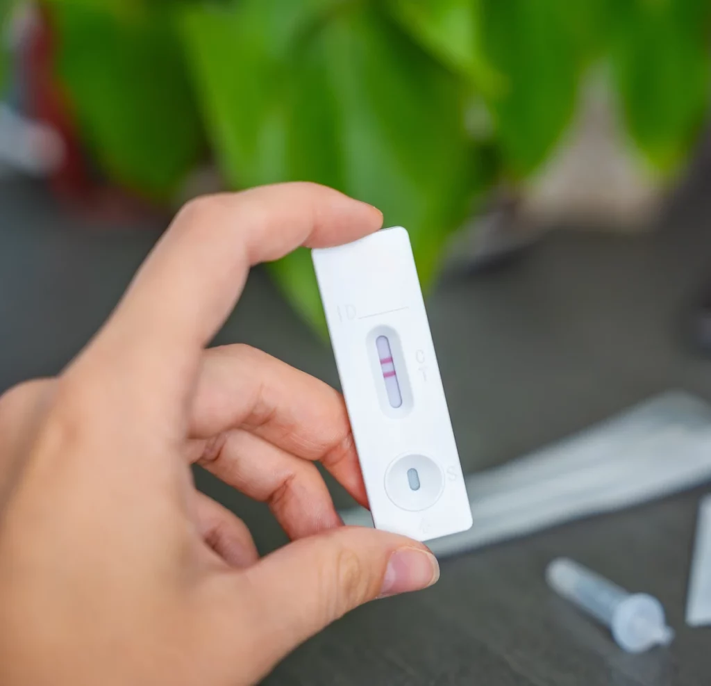 Hand holding a rapid antigen test cassette showing two lines in the result window, indicating a positive result