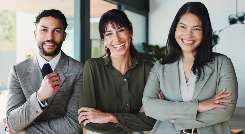 Three smiling business professionals in office attire standing together with arms crossed